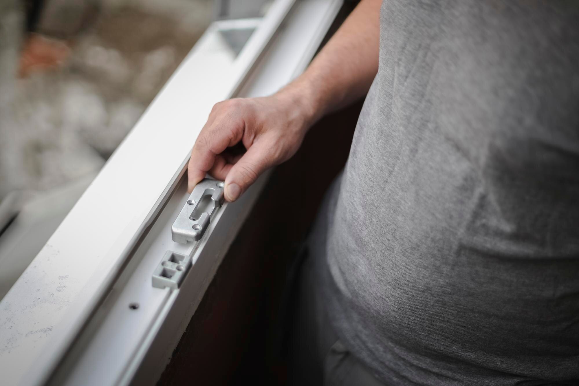 Close-up of a hand operating the latch on a white sliding window frame