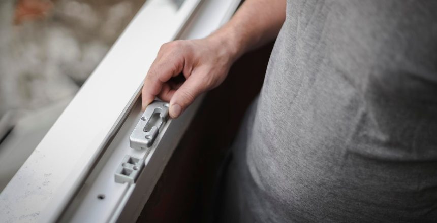 Close-up of a hand operating the latch on a white sliding window frame